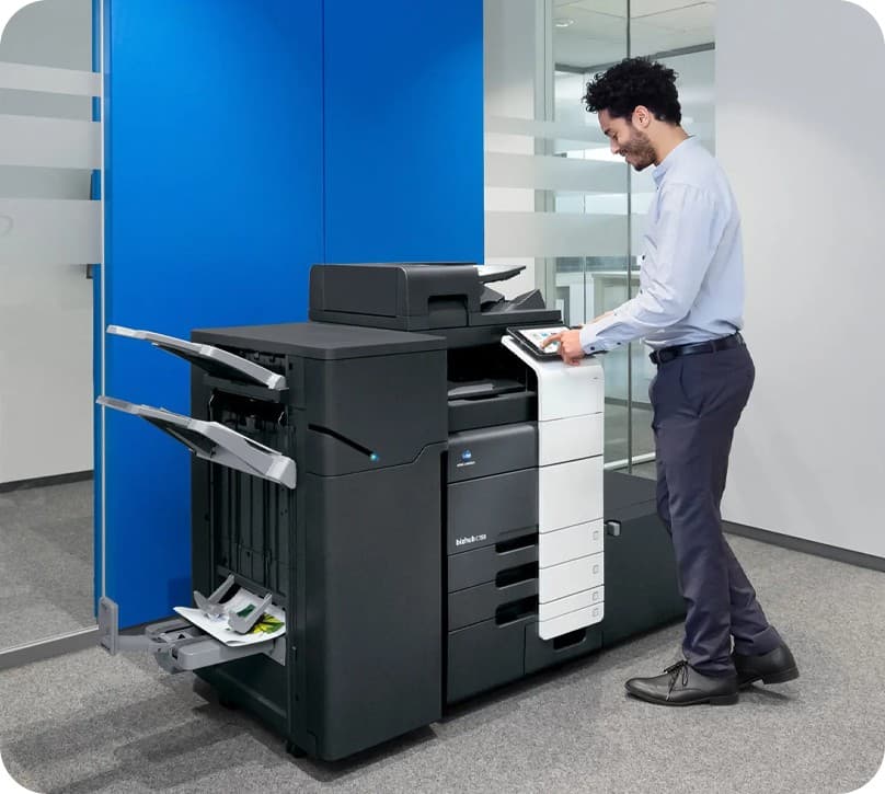 A member of staff using a Konica Minolta bizhub multifunction printer in a modern office