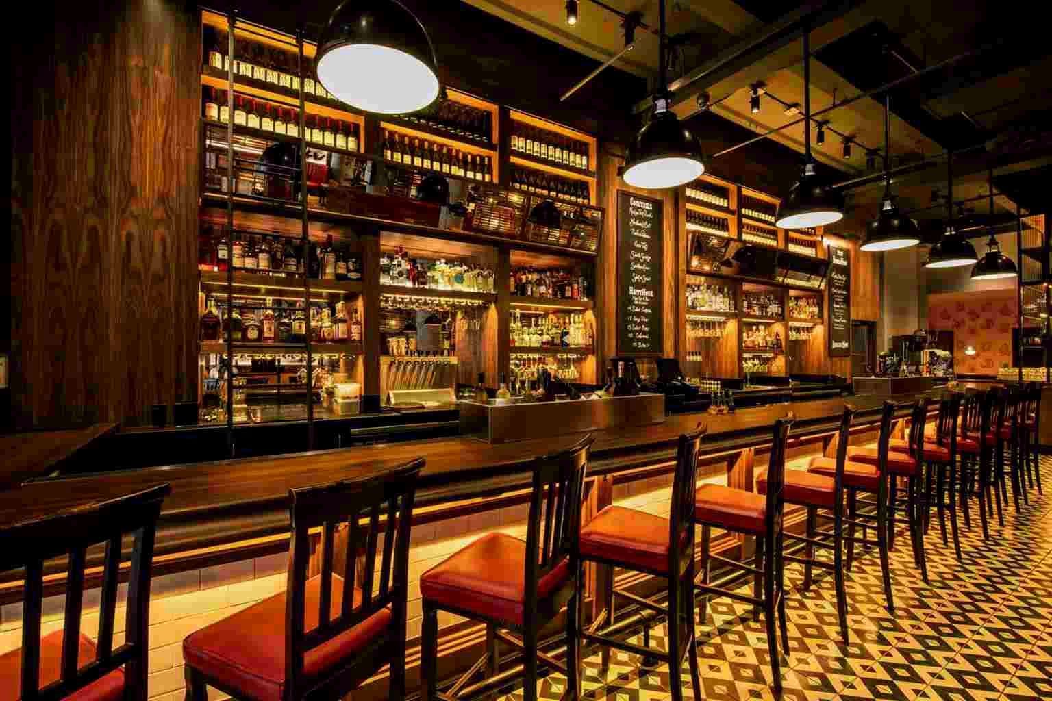 Restaurant bar with backlit shelves of bottles, black pendant lamps and red leather bar stools