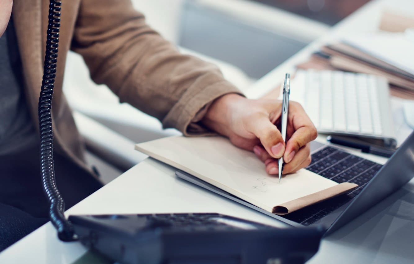 A business desk phone beside a notepad and laptop